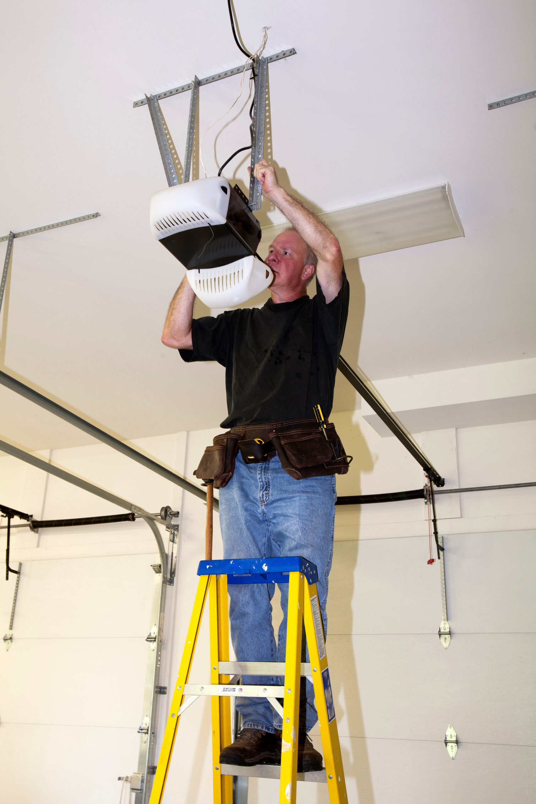 Man standing on a ladder fixing a mechanical garage door opener Albuquerque Custom Garage Door Installation