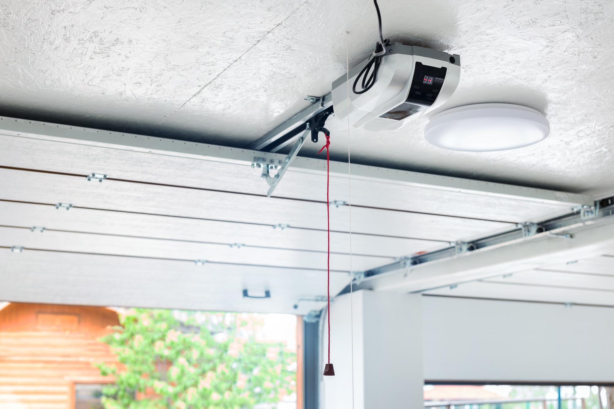 Opening door and automatic garage door opener electric engine gear mounted on ceiling with emergency cord. Double place empty garage interior with rolling entrance gate Albuquerque Garage Door Repair and Adjustment